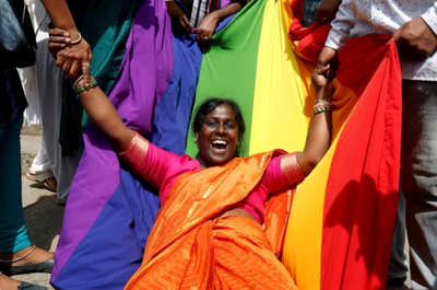 Happy woman wearing a sari in celebration in front of a pride flag!