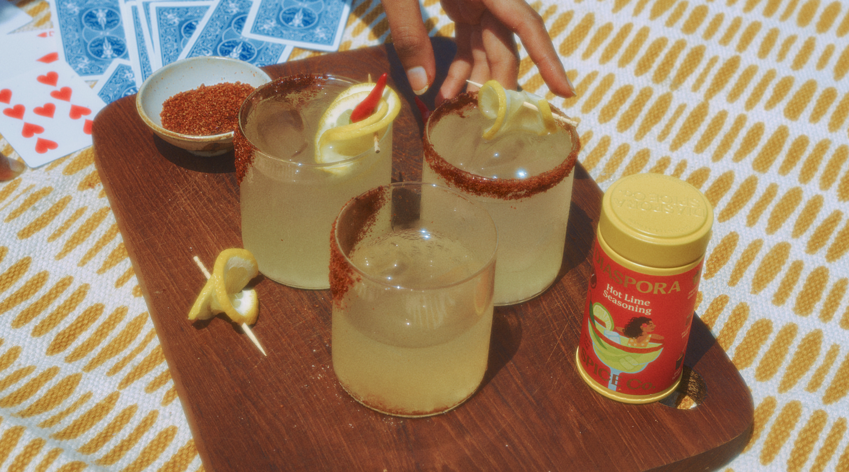 Hot Lim Seasoning tin kept on a picnic blanket along with 2 margarita glasses with a cocktail rim.